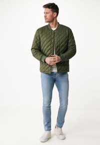 Prošívaná olivově zelená bomber bunda se zapínáním na patentky, žebrovanými manžetami a lehkým designem, kombinována se světle modrými džínami a bílými teniskami.