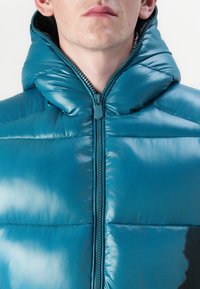 Teal puffer jacket with a high collar, made of shiny material. Features zip closure and quilted sections for insulation.