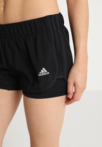 Pantalones cortos atléticos negros confeccionados en una tela texturizada, con una cintura elástica y un acento del logo blanco de Adidas en el lado izquierdo.