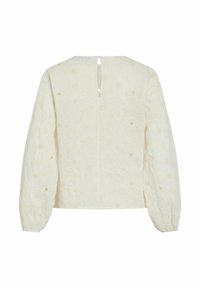 Blouse longue à manches longues crème avec broderie florale ajourée, fermeture à bouton en forme de goutte au dos, et poignets légèrement froncés.