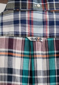 Camisa de cuadros en azul, verde y burdeos. Material de algodón con patrones de franjas variados. Presenta una etiqueta de GANT en el cuello.