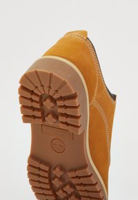 Hnědé semišové boty bez šněrování s texturovanou gumovou podrážkou, vyznačující se vzorem dezénu a kontrastním bílým švem podél švů.