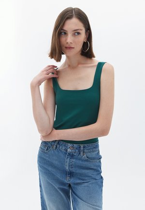 Débardeur vert ajusté avec encolure carrée et larges bretelles, associé à un jean en denim bleu clair taille haute. Texture de tissu lisse.
