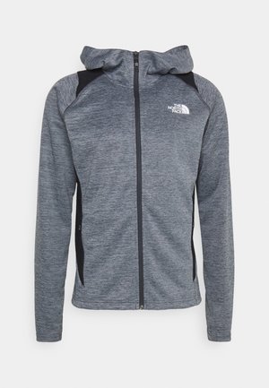 Grijze zip-up hoodie met een zwart accent op de schouders, gemaakt van gestructureerde stof, voorzien van een capuchon en een logo op de linkerborst.