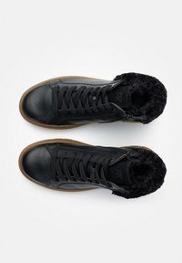 Zapatillas altas de cuero negro con un forro negro peludo, que presentan cordones, un zipper lateral y una suela de goma marrón.