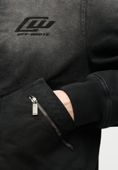 Μαύρο μανίκι φούτερ Off-White με ριμπ μανσέτα, χέρι μέσα σε γωνιακή τσέπη με φερμουάρ που διαθέτει ασημί τράβηγμα φερμουάρ χαραγμένο με το λογότυπο Off-White.