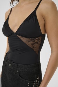 Mujer con una camiseta de tirantes negra con encaje, metida en unos pantalones vaqueros negros de tiro alto con adornos de tachuelas metálicas.
