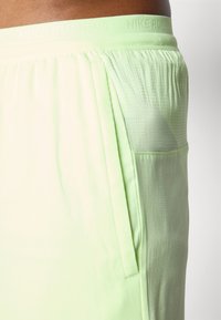 Pantaloni da corsa verdi con una fascia elastica testurizzata, tasca laterale e tessuto leggero e traspirante. Design a gradiente sottile.