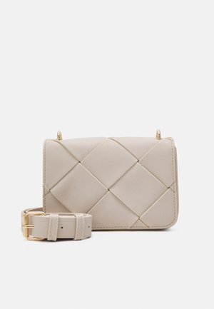 Bolso bandolera beige acolchado con cierre de solapa y correa ajustable y desmontable a juego con hebilla dorada sobre fondo blanco.