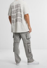 Maglietta oversize in cotone grigio chiaro con grande stampa di lettere a bolle sul retro. Abbinate a pantaloni cargo grigi dal taglio ampio e sneakers bianche.