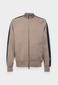 Světle hnědá sportovní bunda na zip s námořnickými akcenty. Obsahuje žebrované manžety, boční kapsy a vysoký límec. Hladká textura látky.