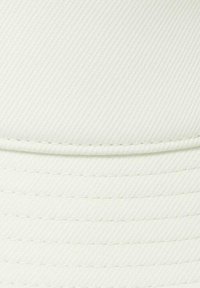 Weiße Mütze aus strukturiertem Stoff mit horizontalen Rippen und sichtbaren Nähten entlang der Krone und des Schirms.