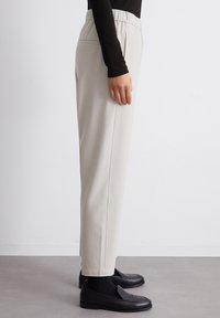 Hellgraue Hose mit elastischem Bund, geradem Bein-Design und seitlichen Taschen, kombiniert mit schwarzen Loafers und dunklen Socken.