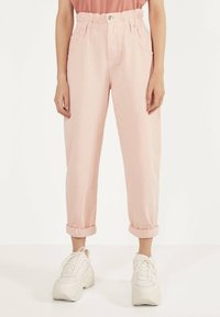 Ljust rosa denimbyxor med hög, elastisk midja. Utrustad med uppvikta fållar, sidofickor och ett silverknappslå. Matchas med vita sneakers.