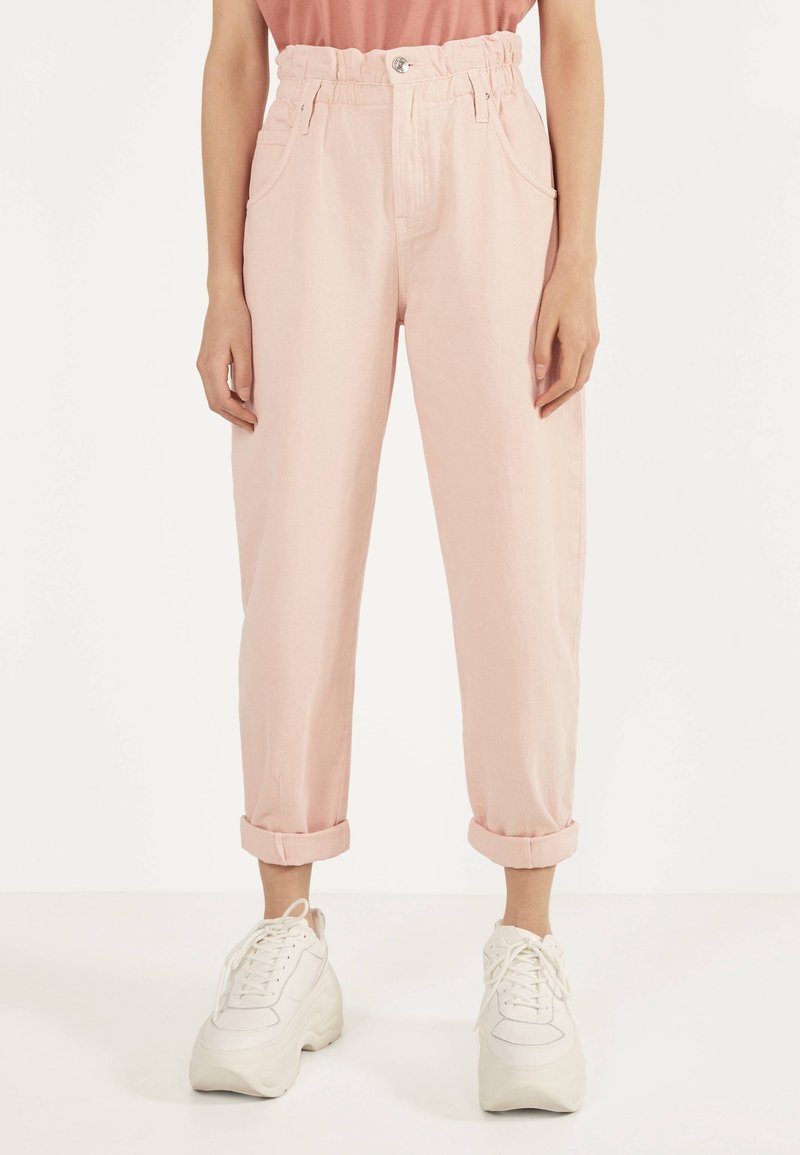 Ljust rosa denimbyxor med hög, elastisk midja. Utrustad med uppvikta fållar, sidofickor och ett silverknappslå. Matchas med vita sneakers.