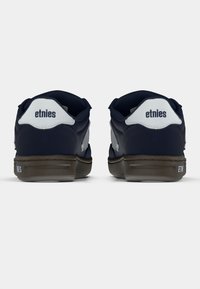 Ναυτικό μπλε παπούτσια σκέιτ με λευκές λεπτομέρειες, διαθέτουν επενδυμένο κολάρο, λογότυπο στη φτέρνα και καφέ καουτσούκ σόλα. Λείος υφασμάτινος σχεδιασμός.