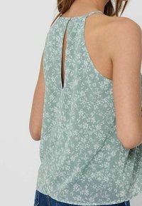 Blouse sans manches vert clair avec motif floral, dos en forme de trou de serrure et tissu doux et translucide. Accentué par une petite fermeture à bouton.