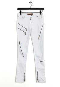 Bílé džíny s několika kapsami na zip, zdobené zlatými kovovými doplňky a úzkým střihem. Látka vypadá lehká a hladká.
