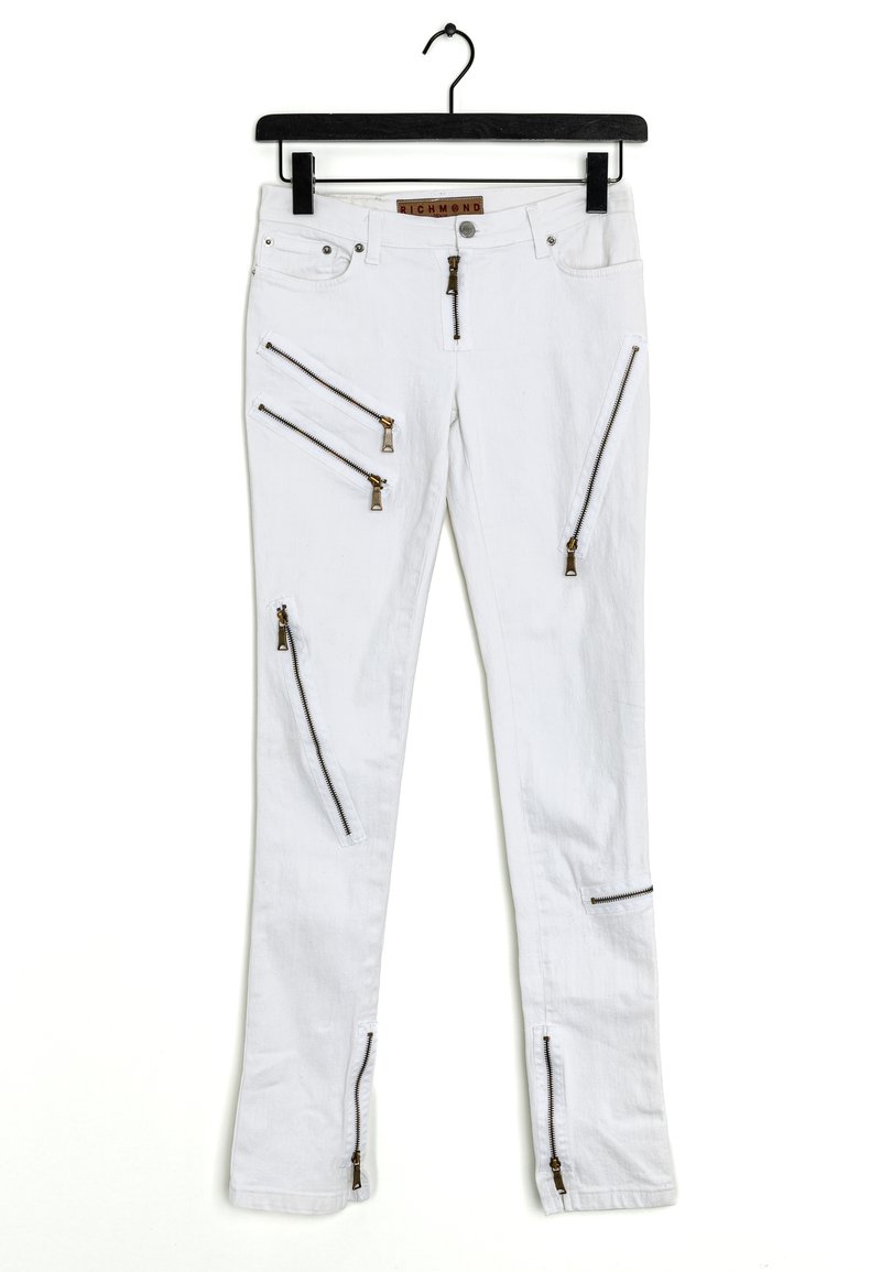 Bílé džíny s několika kapsami na zip, zdobené zlatými kovovými doplňky a úzkým střihem. Látka vypadá lehká a hladká.
