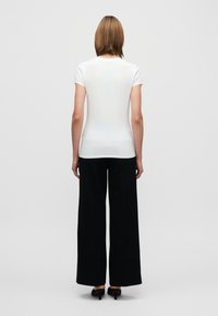 Λευκό τοπ με κοντά μανίκια από απαλό ύφασμα, συνδυασμένο με μαύρο παντελόνι φαρδιάς γραμμής, που δημιουργεί μια αντίθετη εμφάνιση με ελάχιστες λεπτομέρειες.