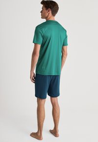 Heren sportoutfit met een teal korte mouwen t-shirt en donkerblauwe shorts, gemaakt van gladde, lichte stof.