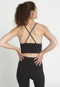 Reggiseno sportivo nero con spalline incrociate, caratterizzato da un tessuto testurizzato e un design di lunghezza media, abbinato a leggings neri a vita alta.