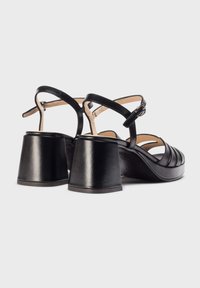 Des sandales en cuir noir présentent un design à large bande, une boucle autour de la cheville et un talon épais et carré pour la stabilité et le style.