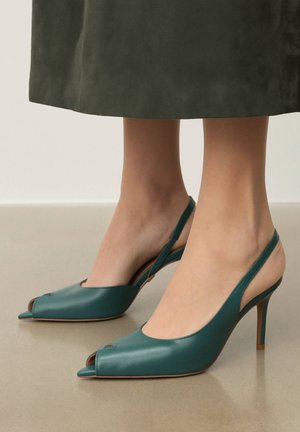 Türkiz bőr pántos magassarkú cipő hegyes orral és nyitott dizájnnal. Fényes felület, vékony tűsarok és kivágott oldalsó díszítések.