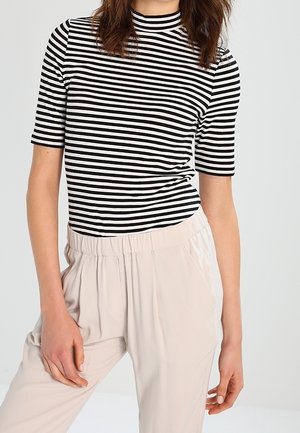 Czarny i biały pasiasty top z krótkim rękawem i wysokim dekoltem, w zestawieniu z jasnobeżowymi spodniami z elastycznym paskiem i bocznymi kieszeniami.