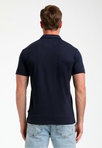 Mornarsko modra polo majica, kratki rukavi, teksturirana tkanina, enobarvna. Priložnostna smer s klasičnim ovratnikom in stranskimi razpoki. Nosimo z svetlo modrimi kavbojkami.