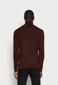 Maglione a collo alto marrone con maniche lunghe, polsini e colletto a coste, realizzato in un materiale morbido, design aderente, texture liscia.