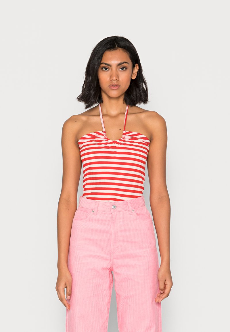 Top de halter com riscas vermelhas e brancas, com uma costura central franzida, combinado com calças de veludo cotelê rosa de cintura alta, com fecho de botão e bolsos.