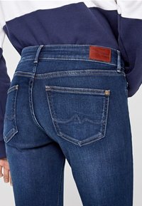 Smala blå jeans i denim, med en läderetikett på baksidan och två bakfickor med enkla sömnadsdetaljer.