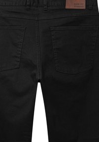 Fekete farmernadrág tiszta, egyszerű fazonnal, közepes derékmagassággal, két hátsó zsebbel és egy barna címkés díszítéssel a derékrészen.