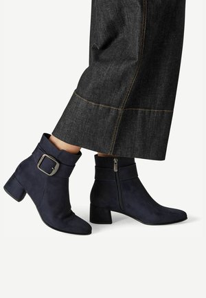 Bottines bleu marine avec fermeture éclair latérale, boucle décorative et talons blocs, portées avec un jean large foncé.