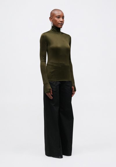 Un top turtleneck verde măslinie, cu un design ajustat, cu mâneci lungi și găuri pentru degete, asortat cu pantaloni largi negri, cu talie înaltă, lejere.