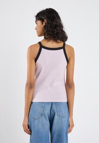 Rosa, ribbet tanktopp med svart kant, med tynne stropper og en tettsittende design. Stoffet har en teksturert overflate. Bredbenet denimjeans synlig.