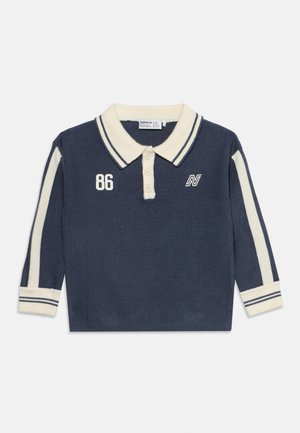 Tmavomodré polo s dlhým rukávom s krémovým golierom a pruhmi na rukávoch, s gombíkmi, číslom 86 a bielym logom na hrudi.