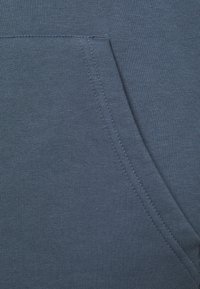 Tessuto blu scuro con una superficie liscia e una tasca frontale. Presenta una cucitura pulita e bordi a coste per una maggiore durata.