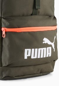 Mørkegrønt rygsæk med en struktureret overflade. Har en lys orange lynlås lomme, stort hvidt "PUMA" logo og en springende pumasilhuet.