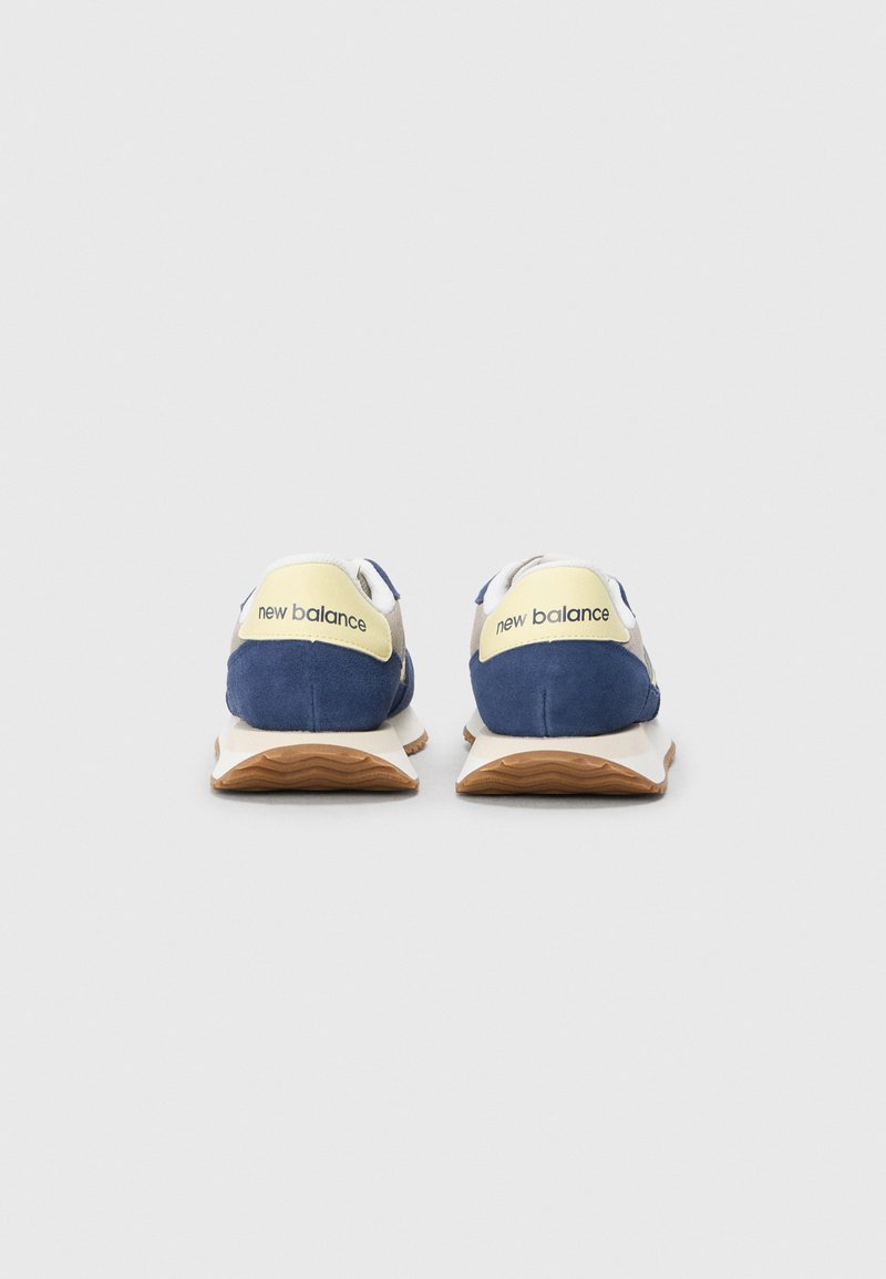 Marineblauwe suède sneakers met witte en gele accenten, voorzien van een gevoerde zool en branding op de hiel.