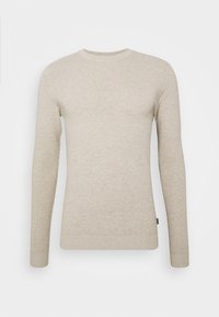 Pull long à manches longues beige clair avec une texture côtelée, un col rond et des poignets ajustés. Présente un motif subtil et une étiquette sur le côté.