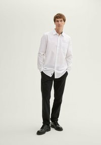 Fehér gombos ing mellzsebbe, fekete nadrággal és fekete cipővel párosítva. Slim fit, sima textúra, letisztult dizájn.