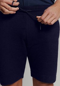 Marineblauwe shorts gemaakt van zachte stof, met een verstelbare trekkoord tailleband en afgewerkte boorden, met een gladde textuur.