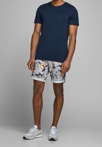 Námořnické bavlněné tričko s kapsou na prsou, kombinované s bílými šortkami s tropickým vzorem palem. Atletické boty v světlé šedé.