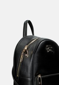 Zaino in pelle nera con hardware in metallo dorato, forma arrotondata e finitura texturizzata. Presenta una maniglia superiore e un logo in rilievo.