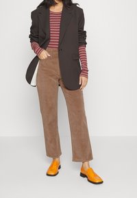 Bruna kordfloddsbyxor, randig långärmad skjorta i mörkröd, överdimensionerad svart blazer och orangea slip-on skor. Enkelt och rent design.