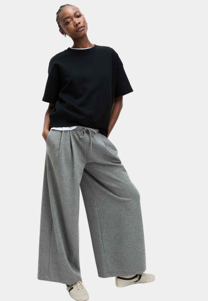 Luźne szare dresy z troczkami w talii i szerokimi nogawkami, połączone z czarną koszulą z krótkim rękawem i białym kołnierzykiem.