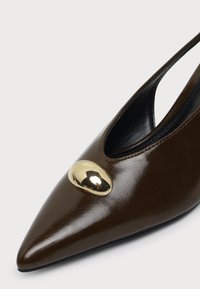 Chaussure slingback en cuir marron à bout pointu avec une décoration ovale dorée brillante sur la partie supérieure avant.