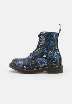 Schwarzer Schnürstiefel mit blau-grünen Blumen- und Totenkopfmuster, gelber Naht an der Sohle und Schlaufe an der Ferse.